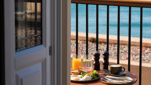 A balcony with a table set for breakfast, overlooking a coastal view with a historic building.