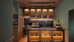 A bar area with wooden cabinets, wine bottles, and a coffee machine.