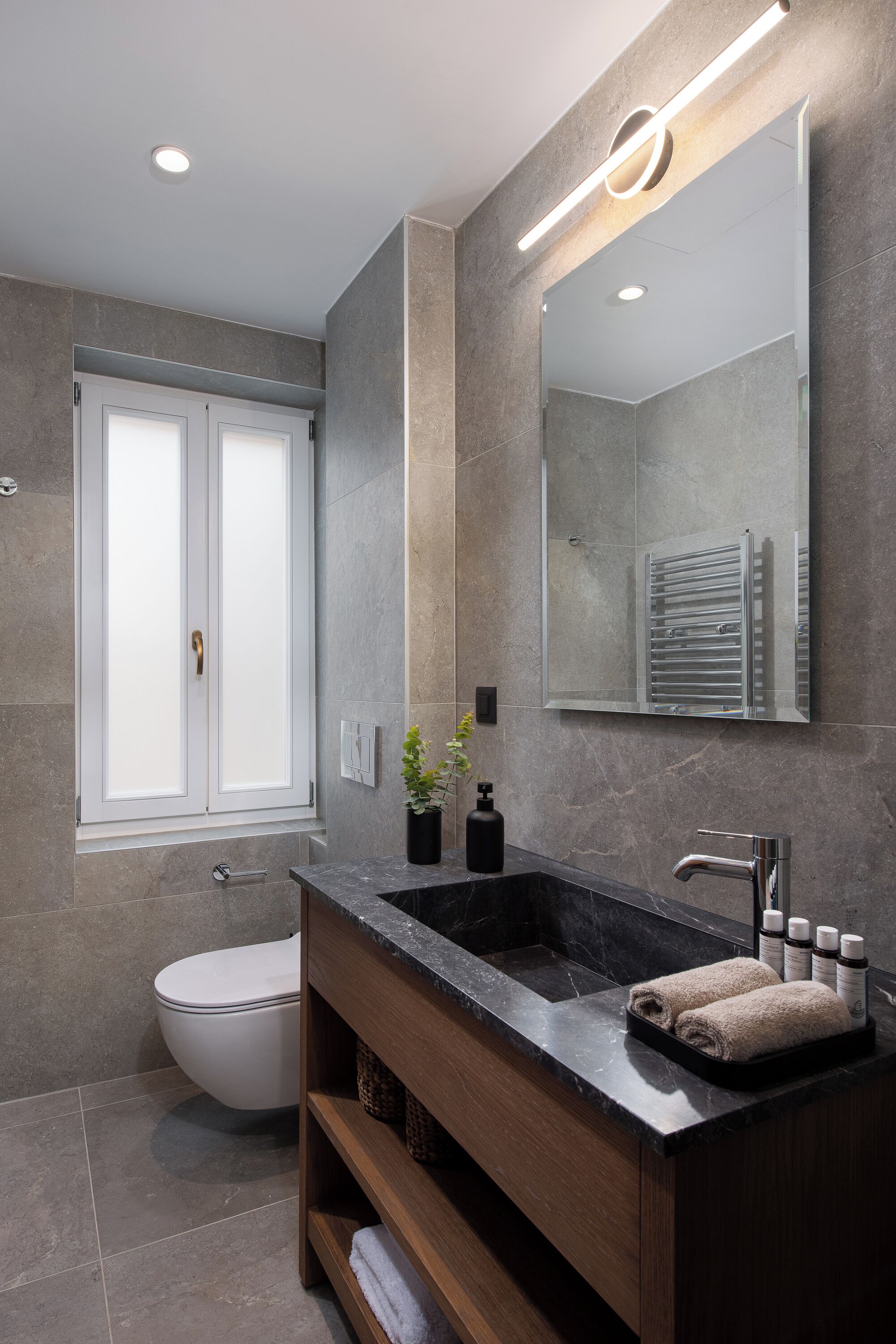 A modern bathroom with a dark marble sink, a large mirror, and a toilet.