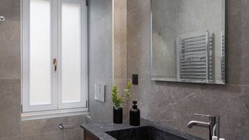 A modern bathroom with a dark marble sink, a large mirror, and a toilet.