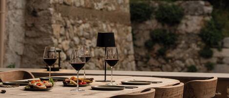 A rustic outdoor dining table with wooden chairs, set against a stone wall backdrop.