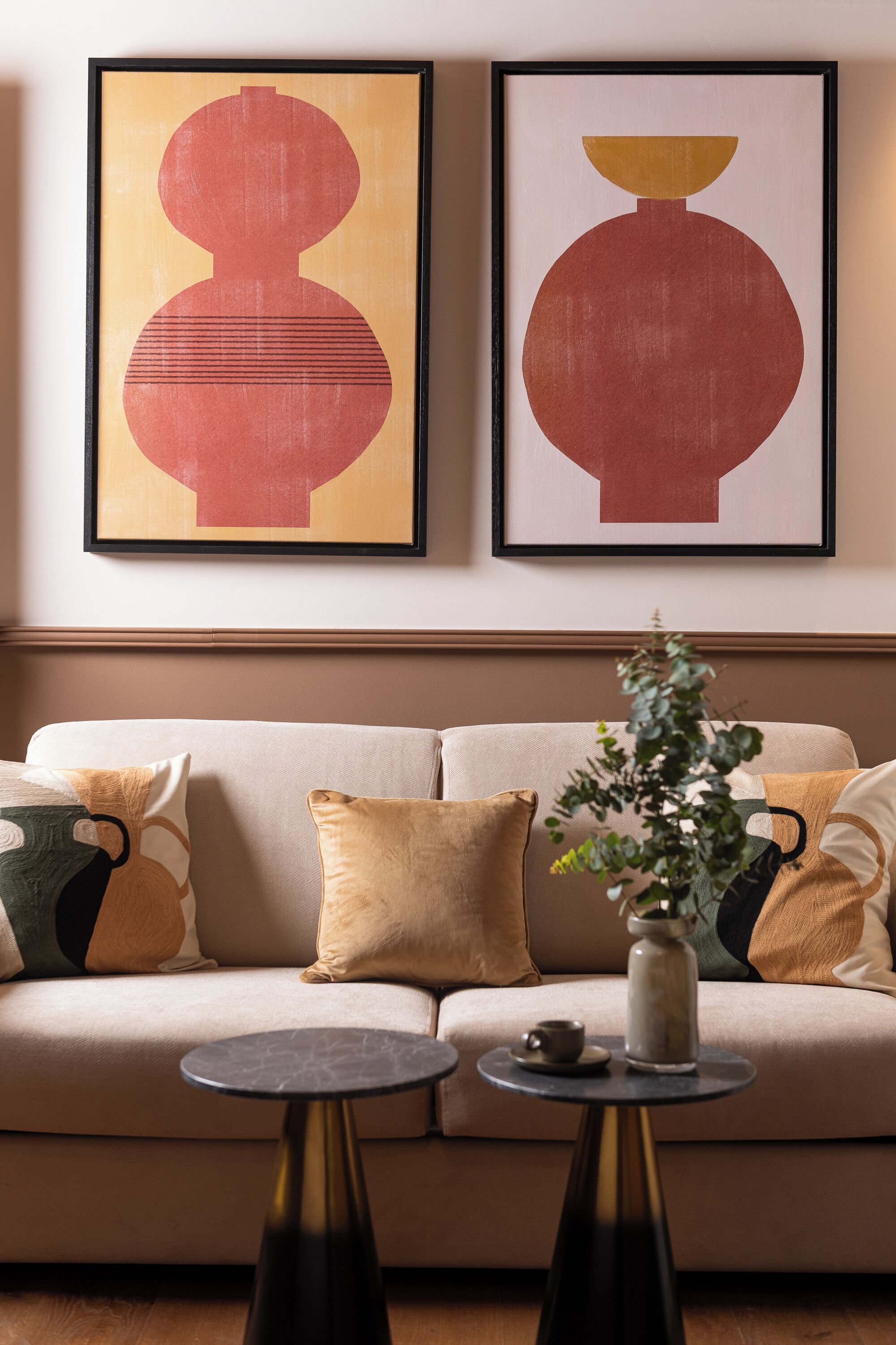 A living room with a beige sofa, two black coffee tables, and two abstract paintings on the wall.