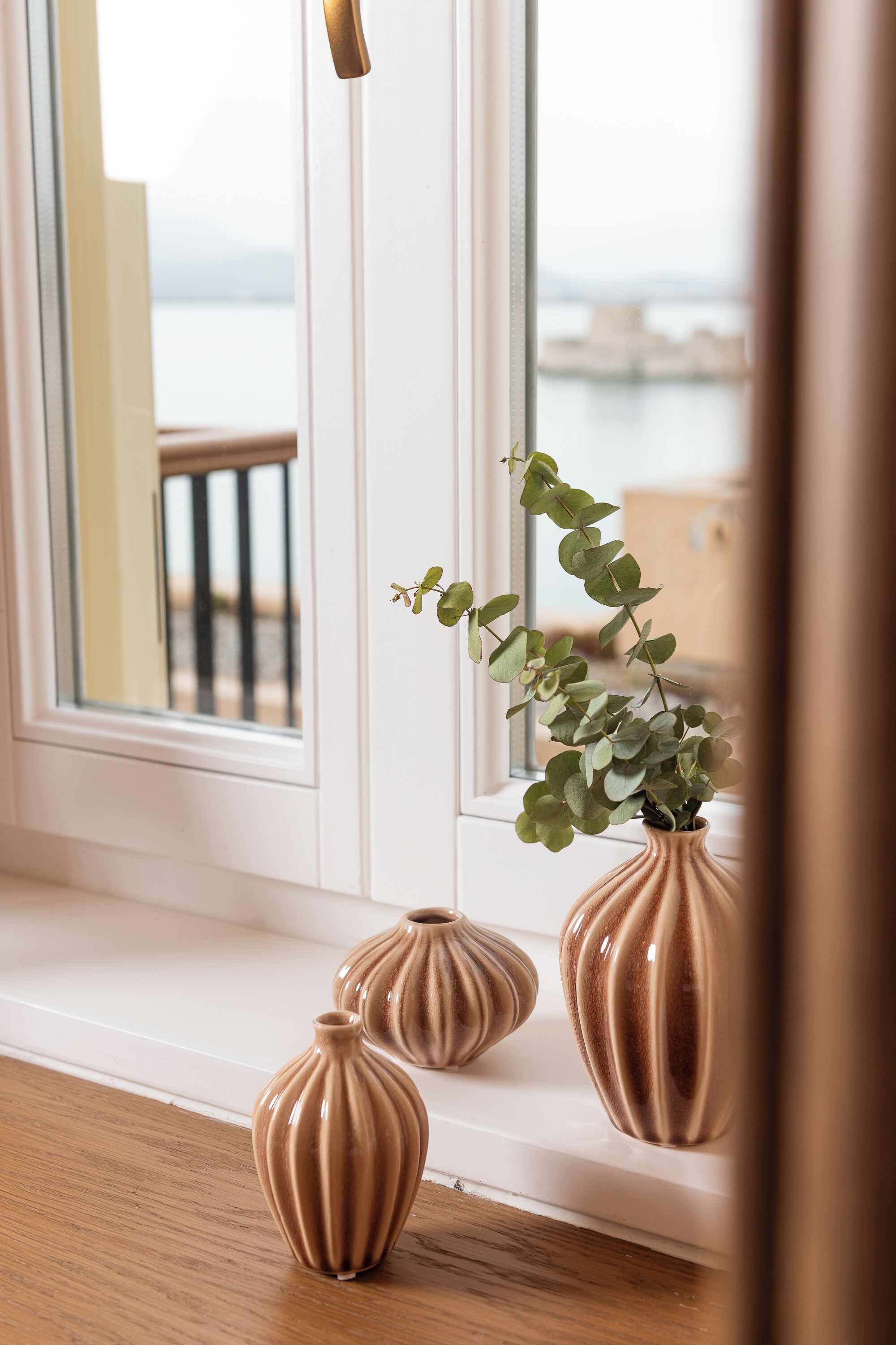 A window sill with three brown vases and a plant.