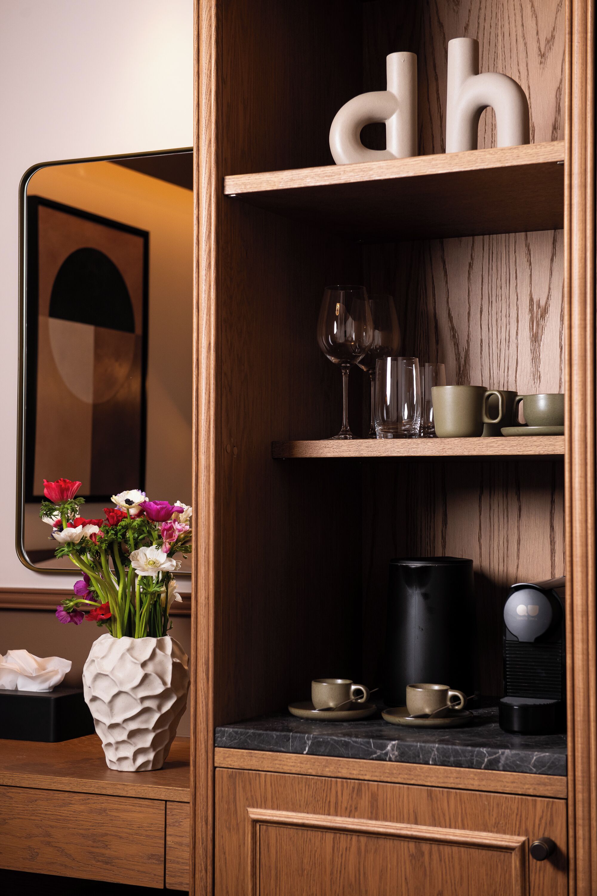 A wooden cabinet with shelves holding cups, a vase with flowers, and a coffee maker.