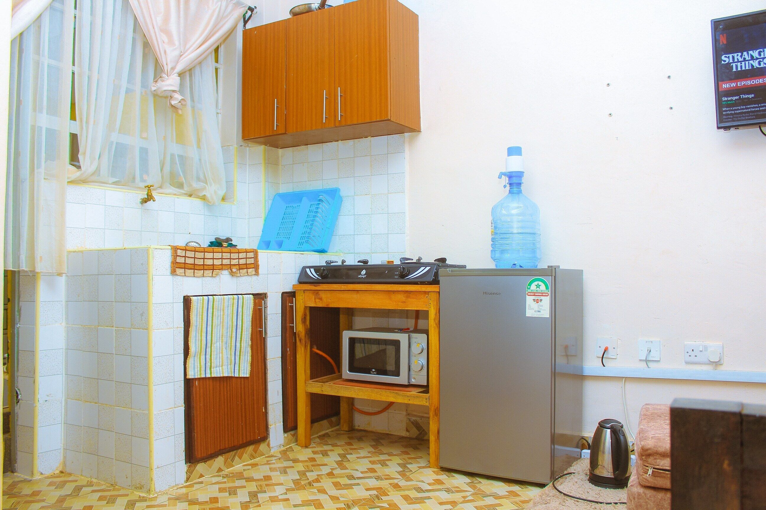 Una cucina compatta con un forno a microonde, un piccolo frigorifero, un dispenser di acqua e un armadietto in legno.