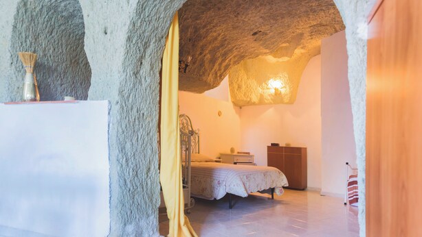 A bedroom with a stone ceiling, a bed with a floral bedspread, a bedside table, and a lamp. - Appartamento in pietra di tufo verde Ischitana, Forio (Forio)