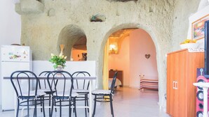 A cozy interior with a stone archway, a dining area with chairs and a table, a wooden cabinet, and a bed in the background. - Appartamento in pietra di tufo verde Ischitana, Forio (Forio)