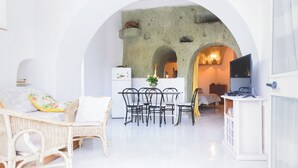 A bright, open-plan living area with a stone wall, a dining table with chairs, a sofa, and a television. - Appartamento in pietra di tufo verde Ischitana, Forio (Forio)