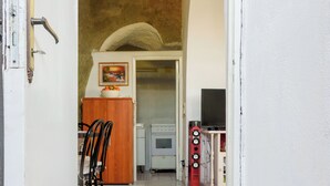 An open doorway leading to a kitchen with a tiled floor, a wooden cabinet, a television, and a red speaker. - Appartamento in pietra di tufo verde Ischitana, Forio (Forio)
