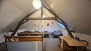 Ein gemütliches Schlafzimmer im Dachgeschoss mit geneigter Decke, Holzbalken, einem Schlafplatz in erhöhter Lage, einem Esstisch und einer kleinen Sitzecke.