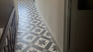Ein Flur mit gemusterten Bodenfliesen, einer Holztreppe und gerahmten Bildern an der Wand.