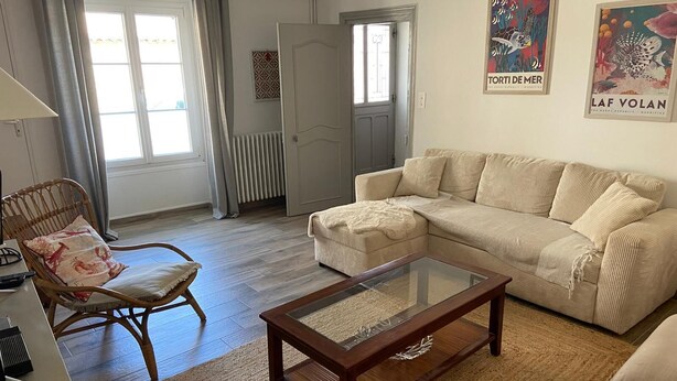 Ein Wohnzimmer mit einem beigen Sofa, einem Holztisch, einem Korbstuhl und einer Heizung.