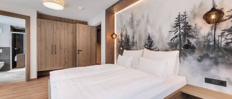 A modern bedroom with a large bed, wooden wardrobe, and a forest-themed wall mural.
