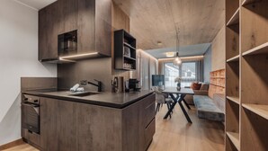 A modern kitchen with dark wood cabinetry, a built-in oven, and a dining area with a wooden table and chairs. - Chalet Fliana (Ischgl)