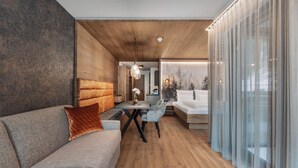 A modern living room with a wooden ceiling, a grey sofa, a dining table with chairs, and a large window with sheer curtains. - Chalet Fliana (Ischgl)