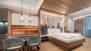 A modern bedroom with a wooden ceiling, a bed with white bedding, a dining area with two chairs, and a wall with a forest mural. - Chalet Fliana (Ischgl)