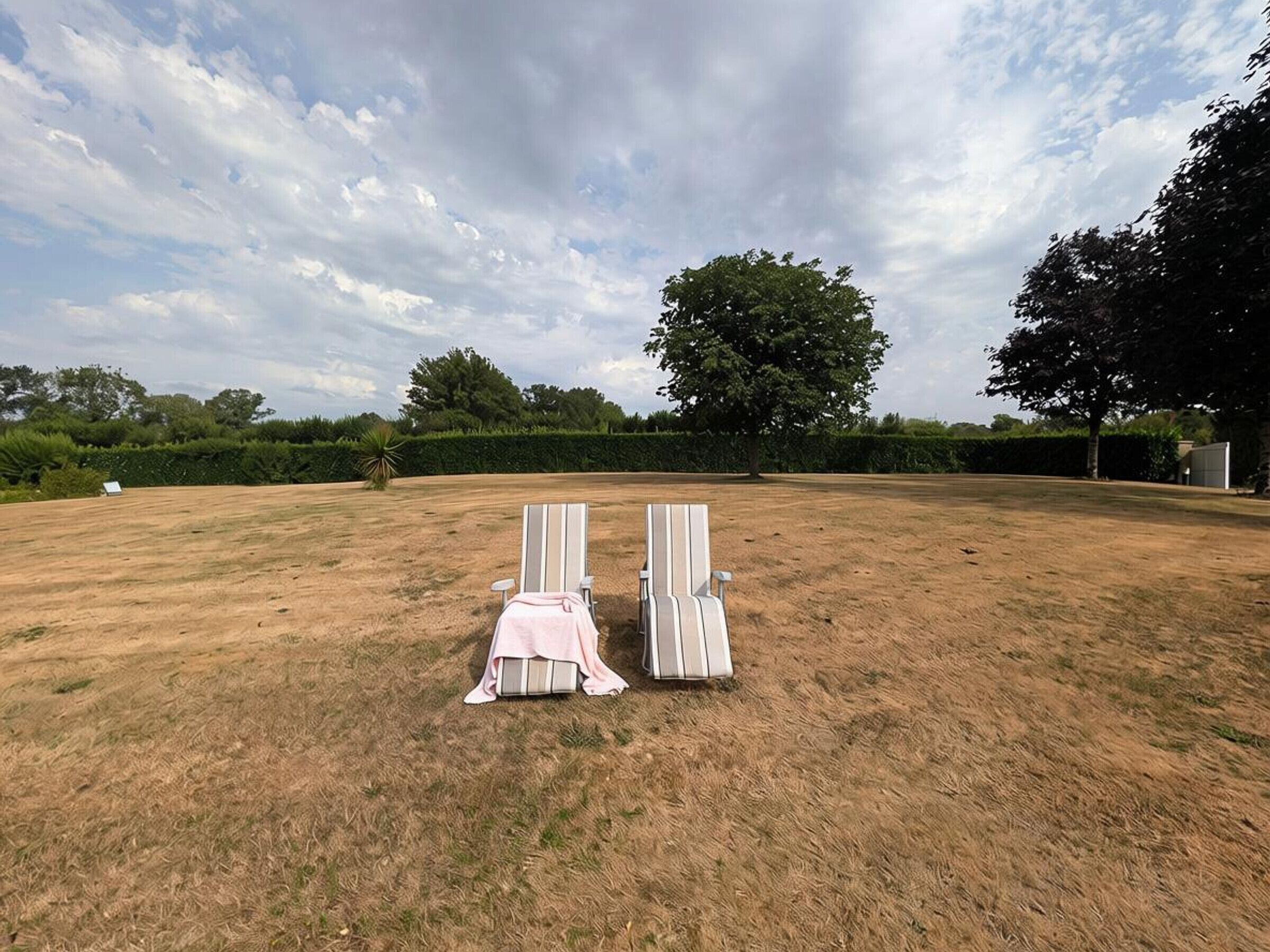 An outdoor seating area with two lounge chairs and a table, surrounded by a grassy field and trees.