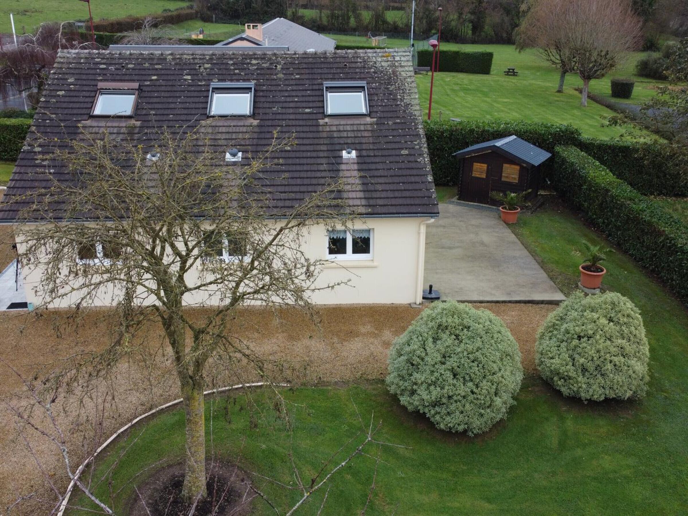 Une maison à deux étages avec un toit en pente, un petit garage attenant et une pelouse bien entretenue agrémentée de deux arbustes ronds.
