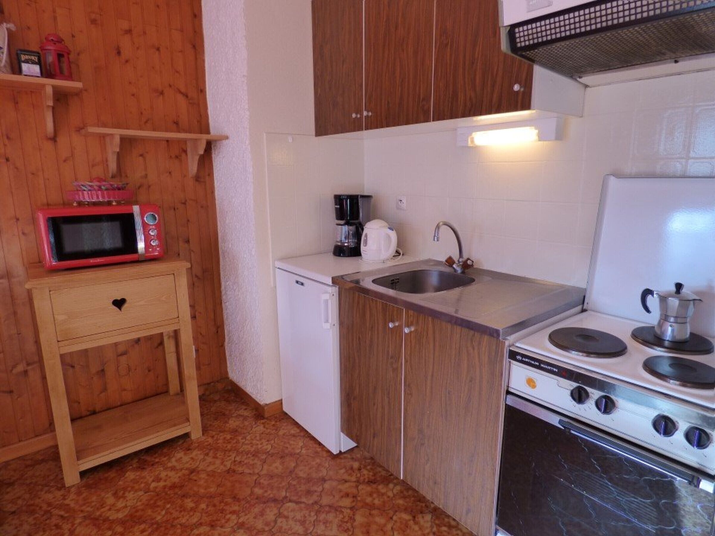 A compact kitchen with wooden cabinets, a white refrigerator, a microwave, a sink, and a stove.