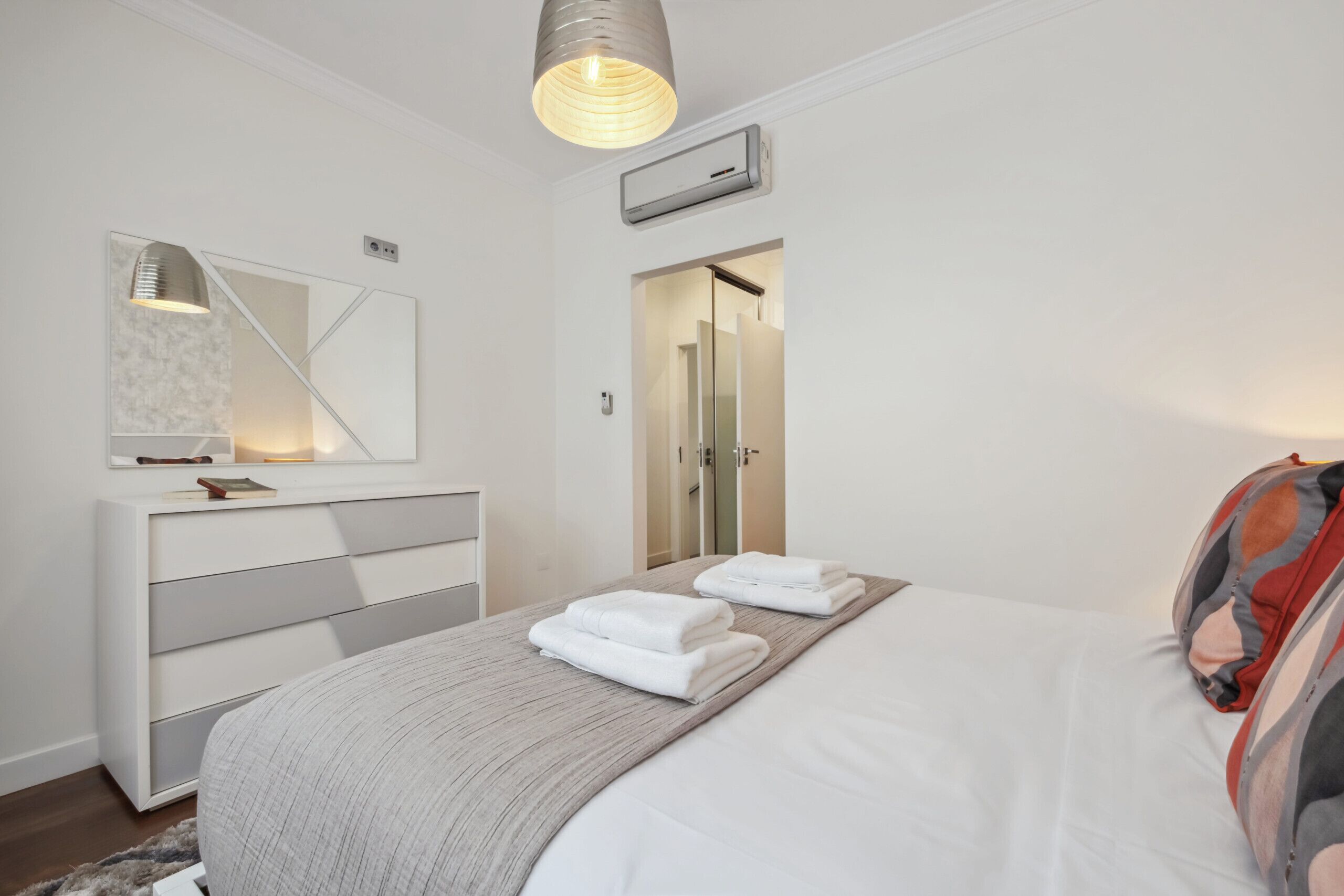 A modern hotel room with a bed, a bedside table, a mirror, and a wardrobe.