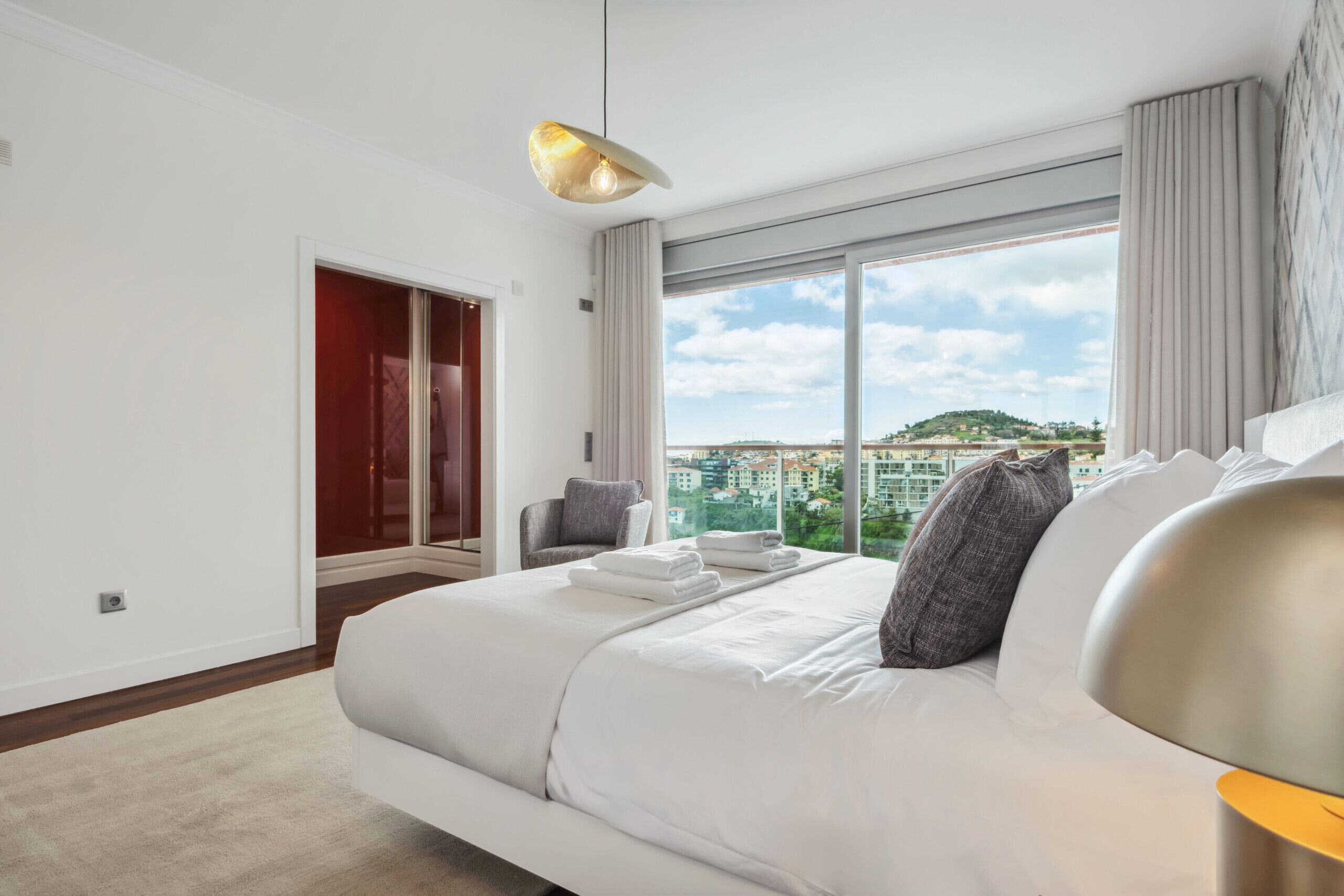 A modern hotel room with a large bed, a view of the city, and a red door.