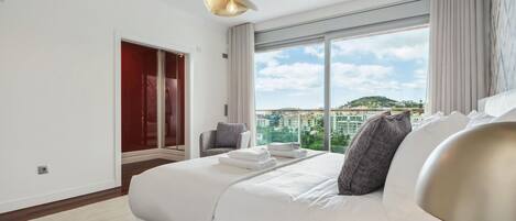 A modern hotel room with a large bed, a view of the city, and a red door.