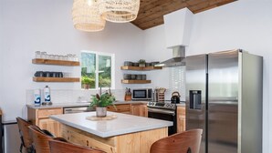 A modern kitchen with a central island, stainless steel appliances, wooden chairs, and a hanging light fixture.