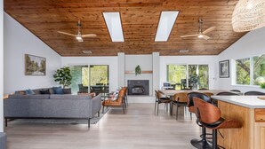 A spacious living area with a fireplace, wooden ceiling, and large windows.