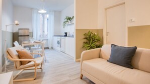 A modern living room with a beige sofa, a wooden chair, a dining table, and a kitchen in the background. - Easylife - Charm & Comfort in Navigli Area (Milano)