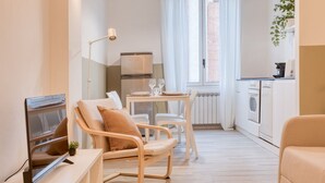 A modern, well-lit living room with a flat-screen TV, comfortable seating, a dining area, and a kitchenette. - Easylife - Charm & Comfort in Navigli Area (Milano)