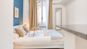A bedroom with a bed, a bedside table with cups and a tray, a window with curtains, and a framed picture on the wall. - Easylife - Charm & Comfort in Navigli Area (Milano)