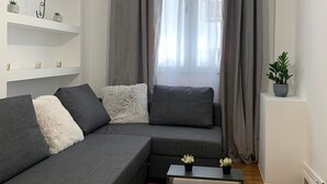 A modern living room with a sectional sofa, a wooden coffee table, and a white shelf with decorative items. - Athenian Stay Kolonaki Apartment (Athens)