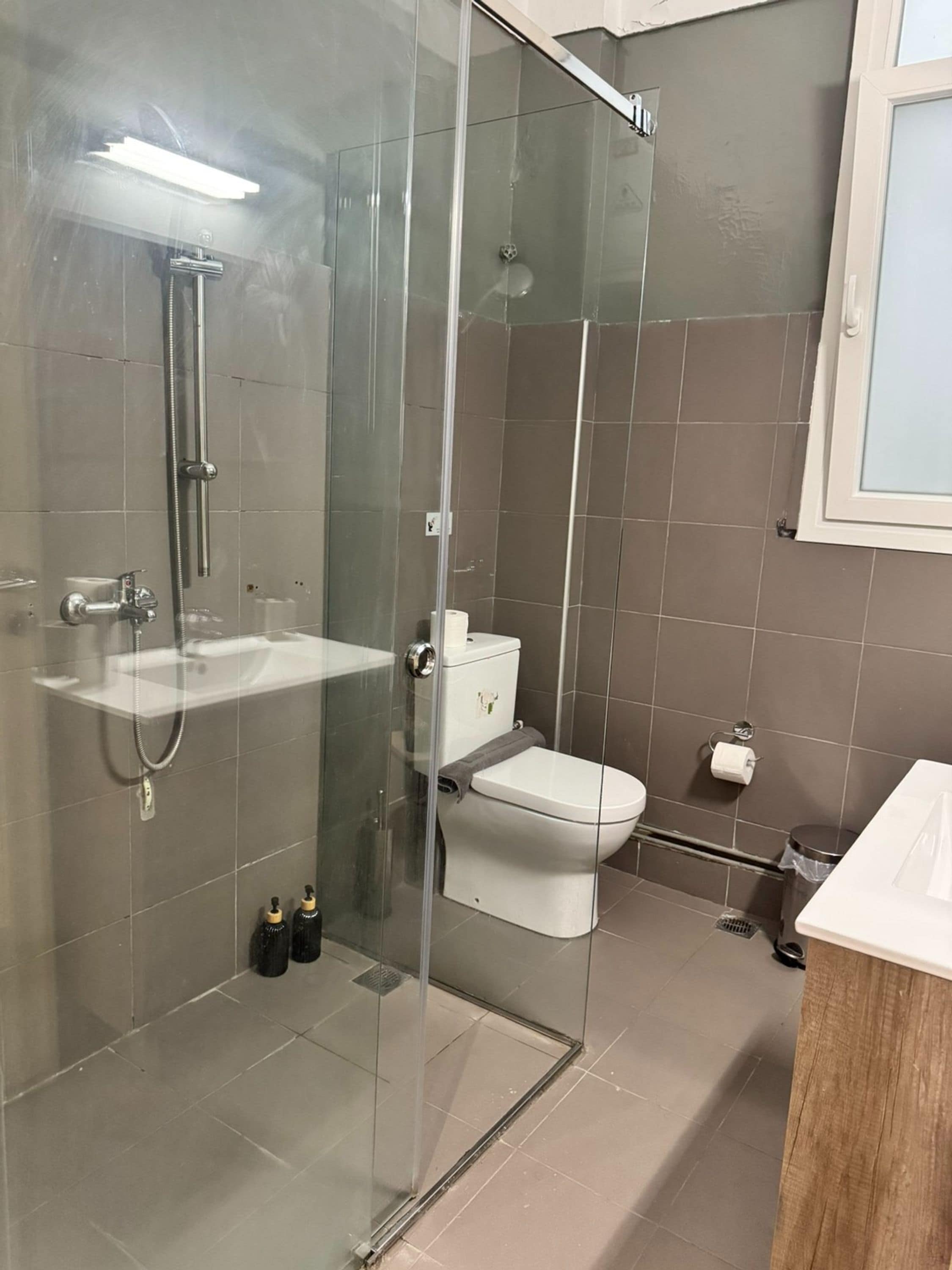 A modern bathroom with a glass-enclosed shower, a white toilet, and a sink.