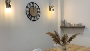 A dining area with a wooden table, white chairs, a wall-mounted clock, and a shelf with a 'WELCOME' sign and plants. - Athenian Stay Kolonaki Apartment (Athens)