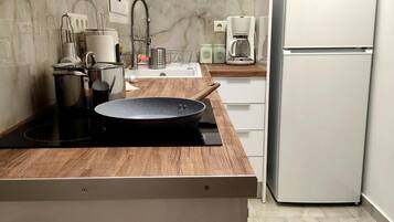 A compact kitchen with a wooden countertop, a built-in stove, a sink, and a white refrigerator.