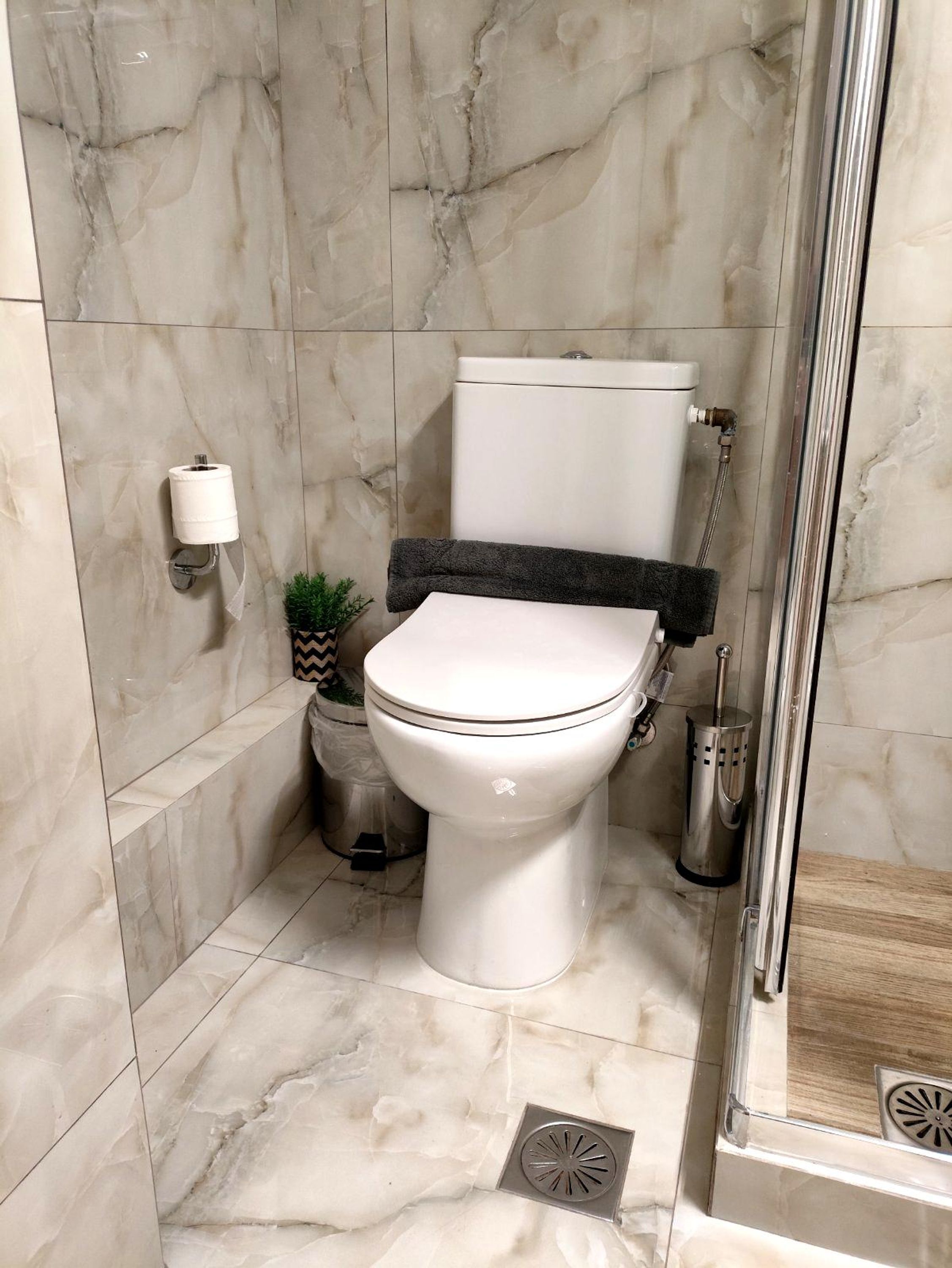 Een moderne badkamer met toilet, douche en een marmeren vloer.