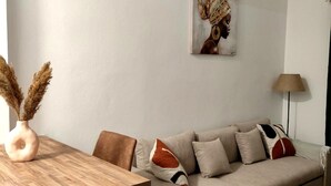 A modern living room with a wooden dining table, a beige sectional sofa, and a painting on the wall. - Athenian Stay Chara s Apartment (Chalandri)