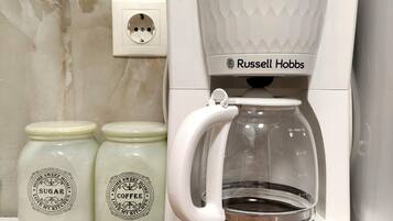Eine Kaffeemaschine mit Glasbehälter, zwei Gläser mit den Aufschriften 'Home Sweet Home Zucker' und 'Home Sweet Home Kaffee', sowie eine Steckdose auf einer Holzoberfläche.