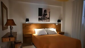 Quarto de hotel bem organizado com uma cama, luminárias de cabeceira, uma mesinha e um quadro pendurado na parede.