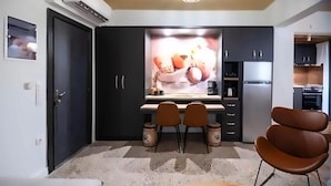 Cozinha compacta com armários escuros, área de refeições com duas cadeiras e luminária moderna.