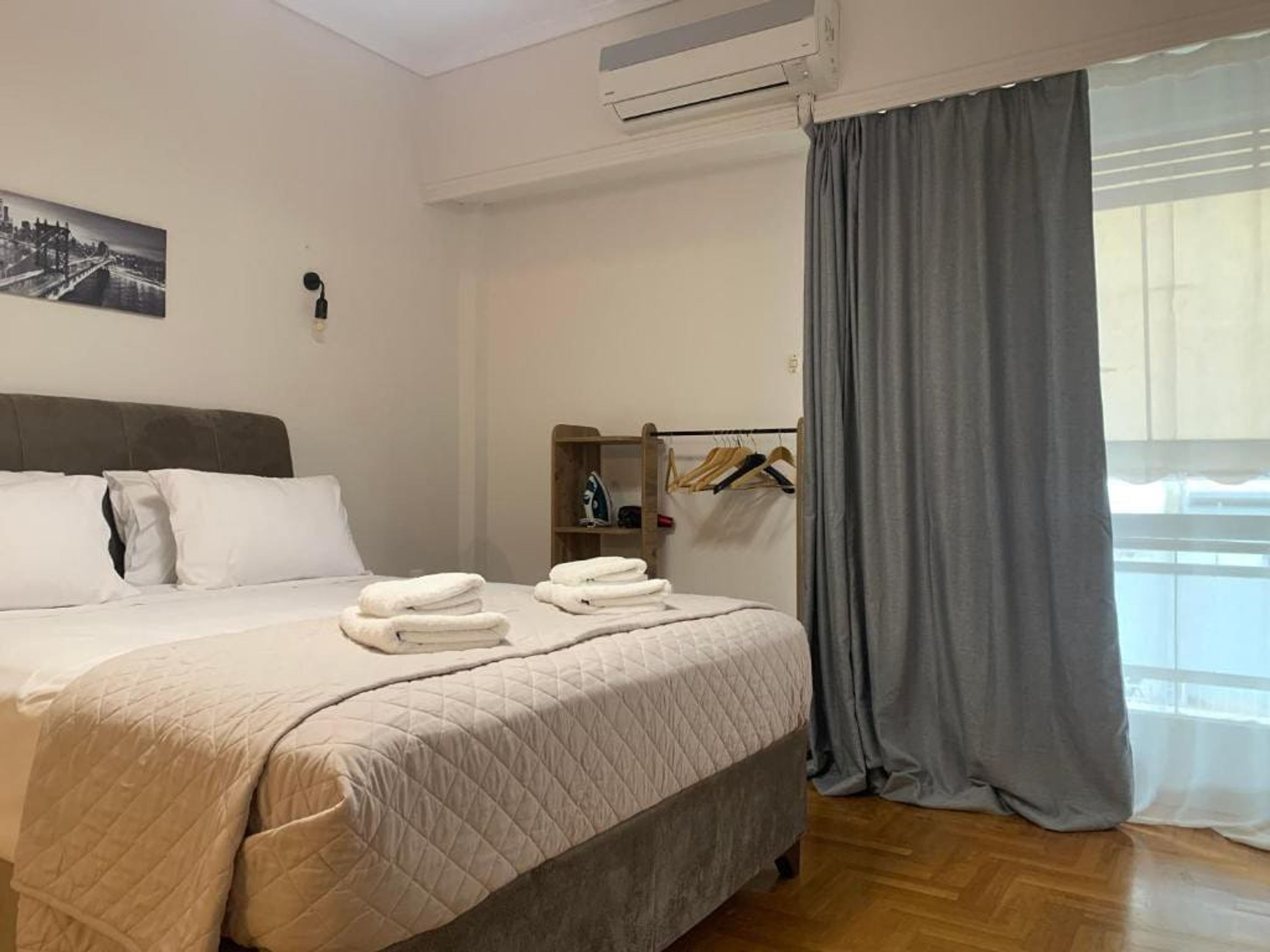 Hotellihuone, jossa on sänky, vaatekaappi, silityslauta ja ikkuna, jossa on verhot.