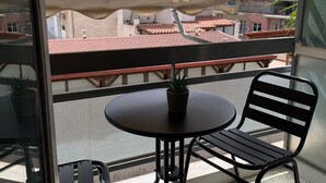 Un balcón con una mesa redonda, dos sillas, una planta en maceta y vistas a edificios con tejados rojos.