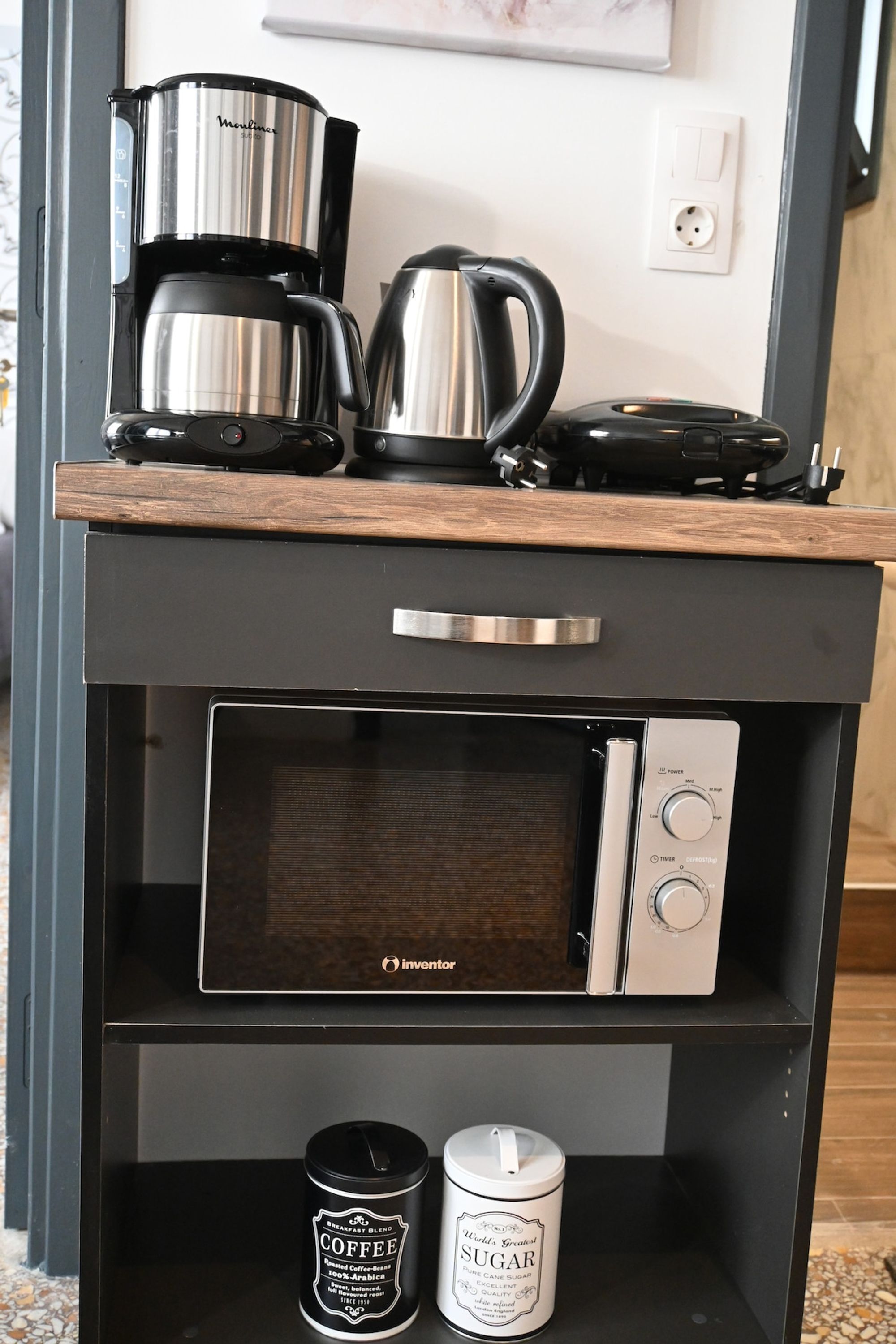 A kitchen area with a coffee maker, kettle, and microwave on a wooden countertop.