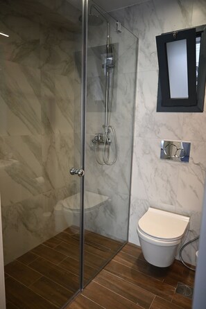 Een moderne badkamer met een glazen douchecabine, toilet en een marmeren wand.