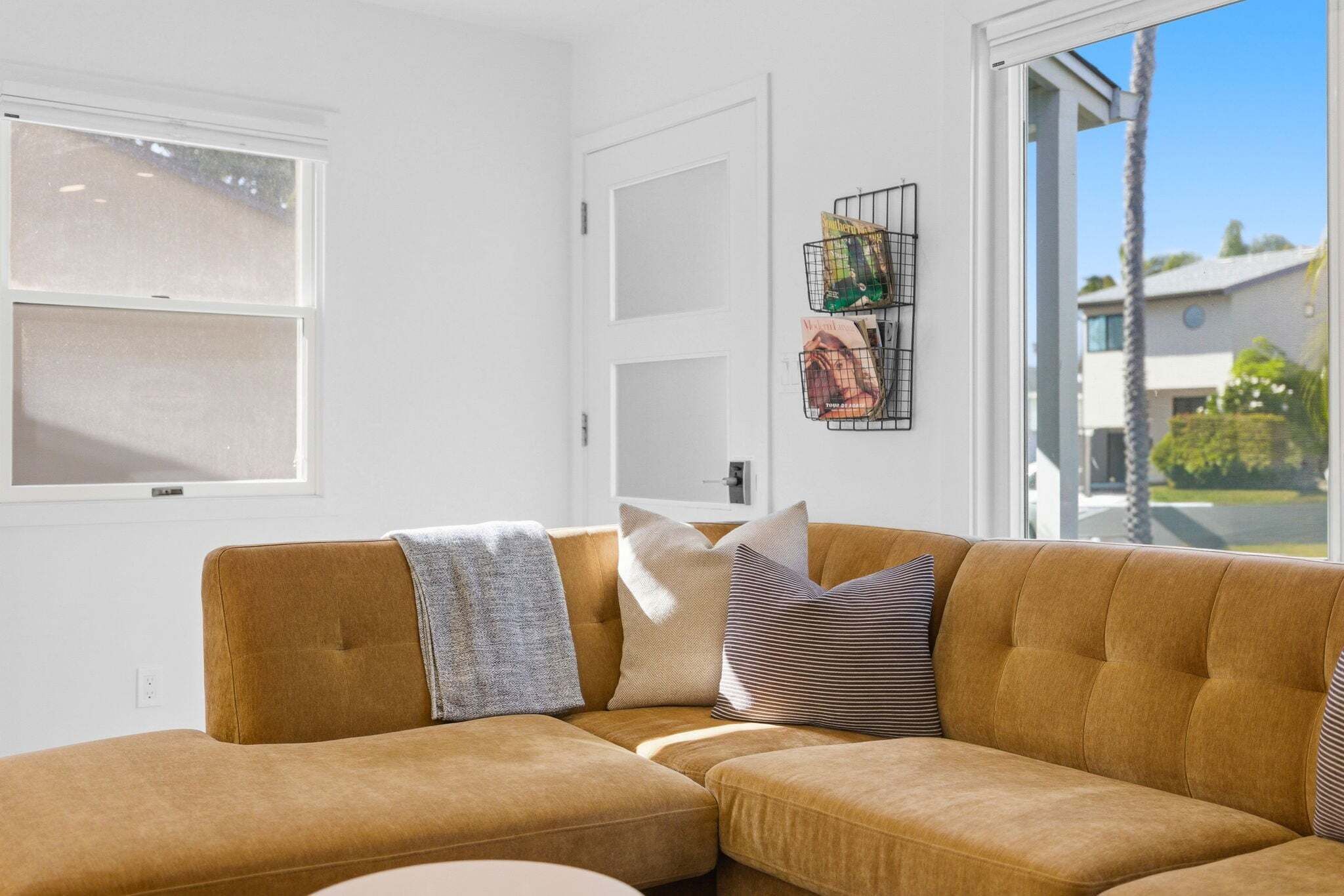 Un salon moderne avec un canap é d’angle marron, une porte blanche et une fenêtre avec des stores.
