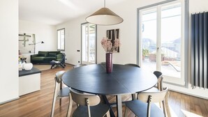 Een moderne eetruimte met een ronde tafel, stoelen en een vaas gedroogde bloemen.