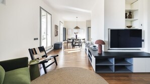 Een moderne woonkamer met een flatscreen televisie, een eethoek met tafel en stoelen, en een bank.