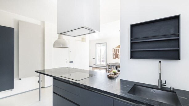 Een moderne keuken met een zwart aanrecht, een inbouwspoelbak en een hanglamp.