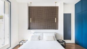 Een moderne slaapkamer met een groot bed, twee nachtkastjes, een wandlamp en een groot raam.