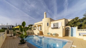 Una piscina con borde de azulejos, plantas en macetas y mobiliario de exterior.